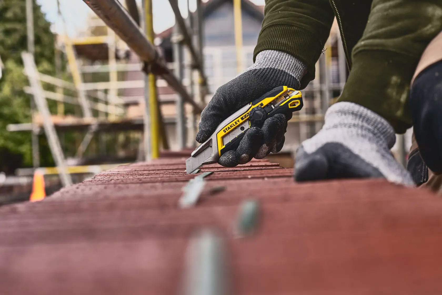 Stanley FMHT10592-0 cuchillo utilitario amarillo y negro, usado por mano enguantada en obra.