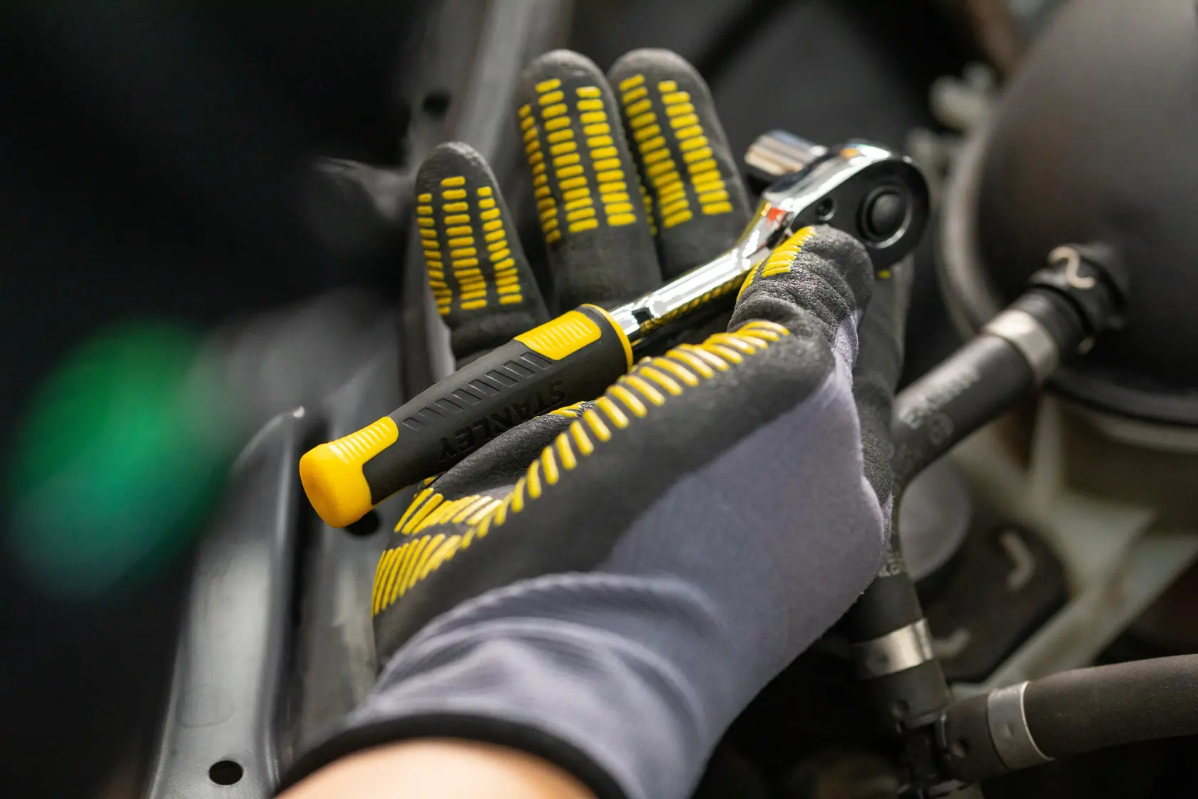 STANLEY STMT82831-LA llave de carraca con mango negro y amarillo en mano enguantada, utilizada para trabajo automotriz.