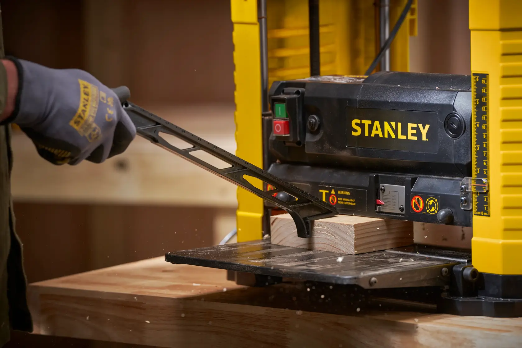 STANLEY STP18-B2 cepillo de banco en uso, vista de cerca de una mano enguantada ajustando una pieza de madera.